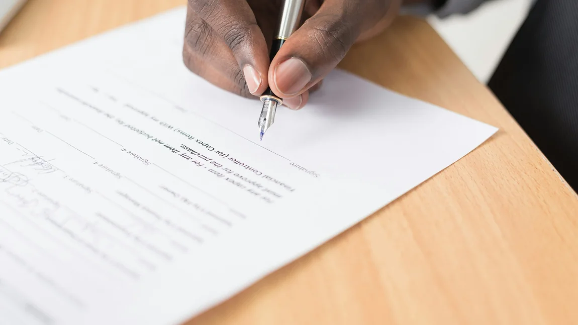 A hand signing a printed document at a desk.